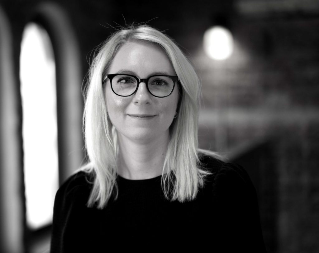 Portrettbilde av Rikke Solberg, kommunikasjonsansvarlig i Fundraising Norge. Hun har på seg sort bluse og står foran et vindu. Bildet er i sort/hvitt.