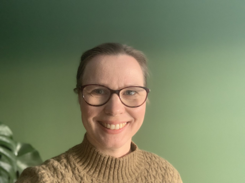Portrettbilde av Ann Kristin Wisløff Nilssen, seksjonsleder marked i Nasjonalforeningen for folkehelsen. Hun har på seg beige, strikket genser og står mot en grønn vegg. 