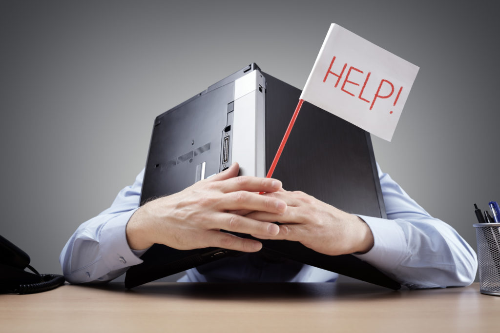 Illustrasjonsbilde av en overarbeidet person som gjemmer seg under en pc og spør om hjelp.