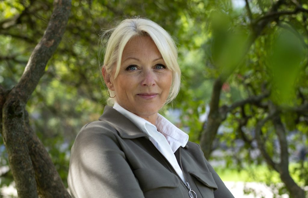 Portrett av Siri Nodland, generalsekretær i Fundraising Norge. Hun har på seg grønn jakke og hvit skjorte, og hun er ute i bybildet. 